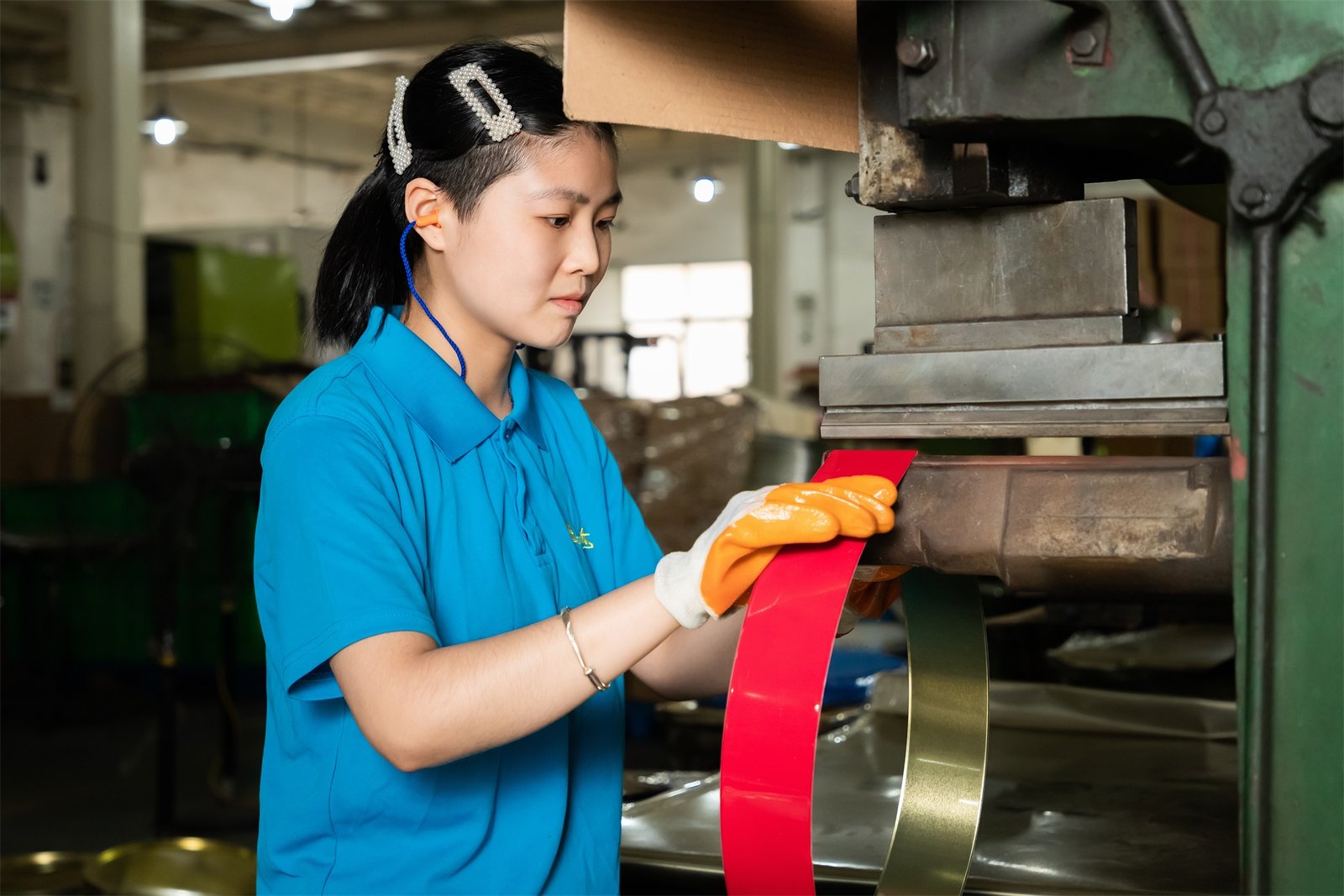 A workshop technician at TDTIN factory performing the precision curling process on a red tinplate strip to ensure smooth, safe edges for high-quality custom metal packaging.
