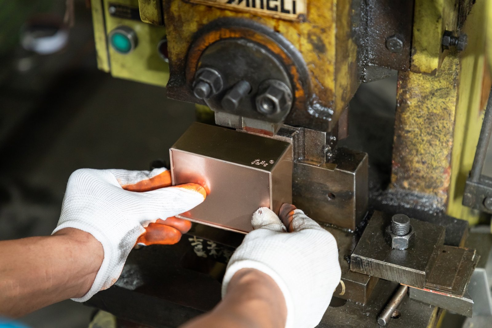 A technician at TDTIN factory using a specialized machine to create a crisp 3D embossed logo on a metallic custom tin box, adding premium texture and brand identity to the packaging.