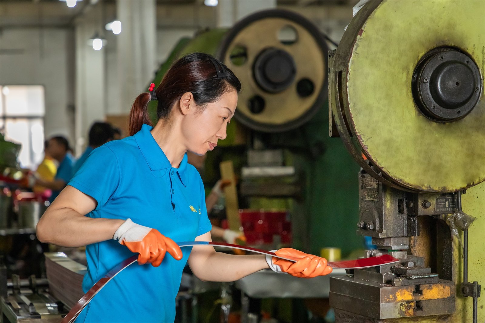 A skilled workshop technician at TDTIN factory performing the precision notching process on a red tinplate strip to ensure perfect alignment and shaping for custom metal packaging.