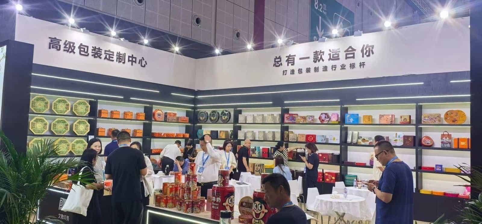 Visitors meeting at tables in the TDTIN exhibition booth with printed tin boxes displayed on shelves