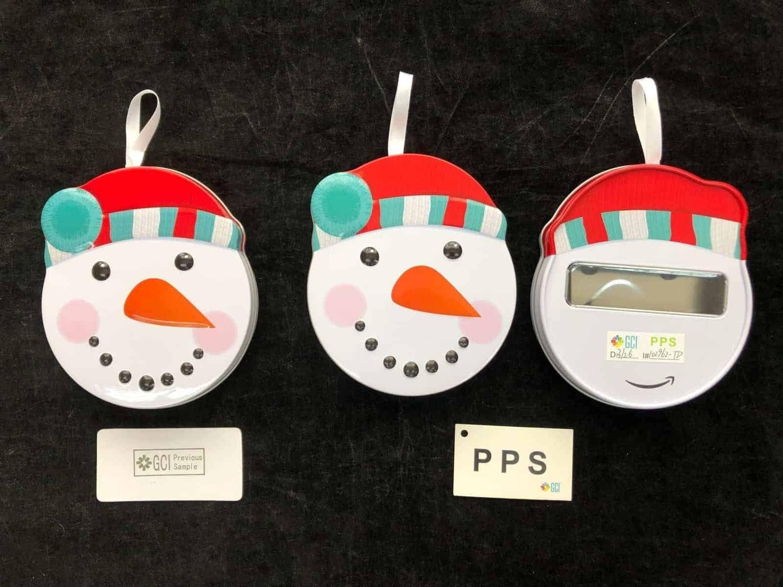 Snowman-shaped tin samples with hanging loops, showing front designs and a rear view for comparison